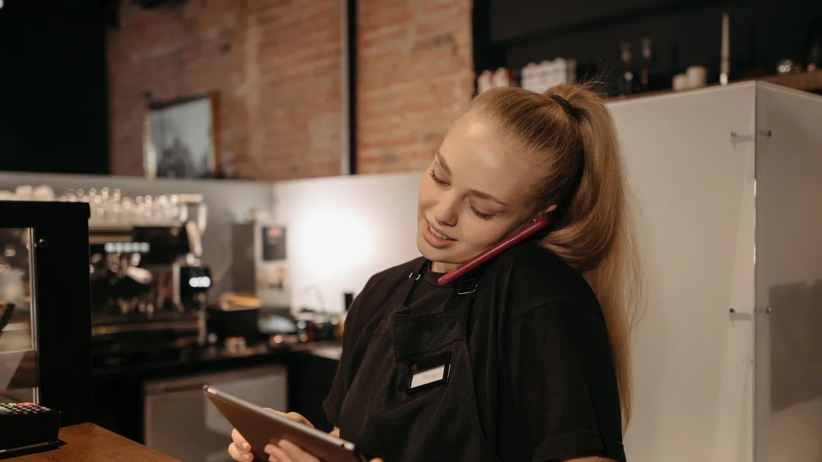 Young worker on a break at a cafe counter filling in a quick cash loans application on her phone